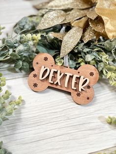 a wooden dog bone ornament with the word dexter engraved on it, surrounded by greenery