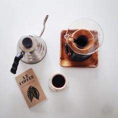 a cup of coffee next to a book and a teapot on a white table