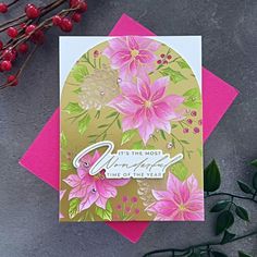 a pink and gold greeting card with flowers on it, next to some red berries