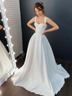 a woman wearing a white wedding dress standing in front of a mirror with her hands on her hips