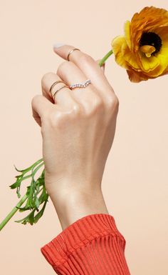 a woman's hand holding a yellow flower in front of her face with the petals still attached