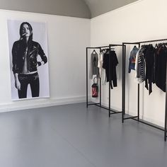 an empty room with clothes on racks and a poster hanging in the wall behind it