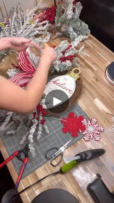 a person is making christmas decorations on a wooden table with scissors and other holiday decor