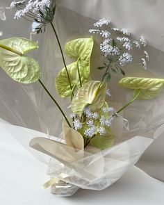 a vase filled with flowers and greenery on top of a white table covered in plastic