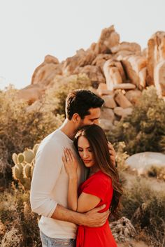 a man and woman embracing each other in front of some rocks with cacti