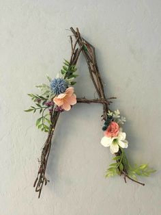 a letter made out of twigs with flowers and leaves on it, hanging from the wall