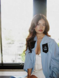 a woman sitting on top of a bed wearing a blue jacket and white dress shirt