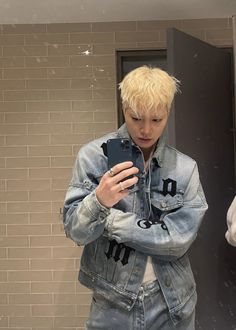 a young man is looking at his cell phone in the mirror while wearing an oversize denim jacket