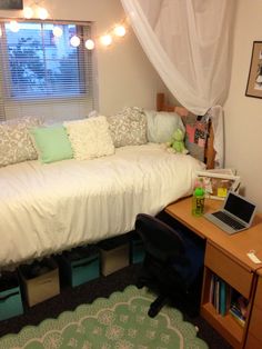 a bed sitting under a window next to a desk with a laptop computer on it