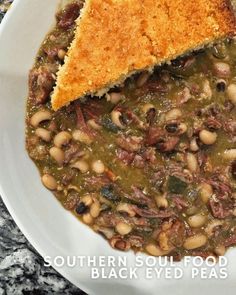 a white bowl filled with beans and meat next to a piece of bread on top of it