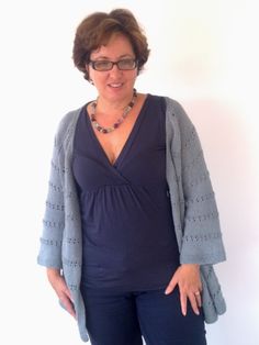 a woman standing in front of a white wall wearing glasses and a cardigan sweater