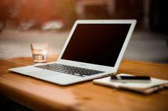 an open laptop computer sitting on top of a wooden table next to a glass of water