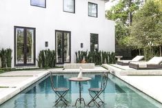 two chairs sitting on top of a pool next to a white house with black windows