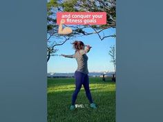 a woman standing in the grass with her arms spread out, holding a sign that says and conquer your fitness goals