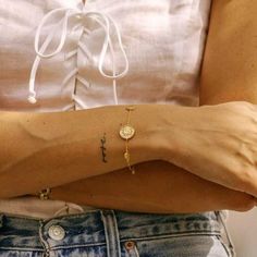 a woman's arm with a cross on it and a coin bracelet attached to the wrist