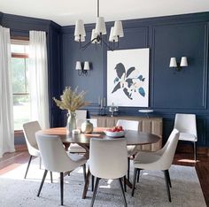 a dining room with blue walls and white chairs around a round table in the center