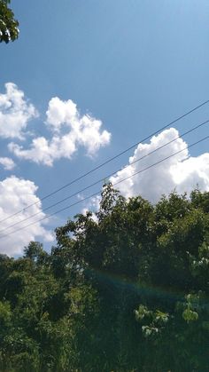 the sun shines brightly through the clouds in the blue sky above some green trees