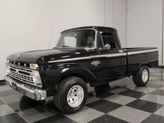 an old black pickup truck is parked in a room with checkered tile flooring