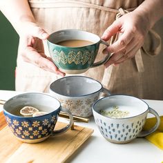 a woman is holding a cup of coffee in front of three bowls on a cutting board