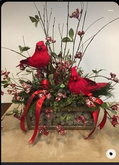 two red birds sitting on top of a wooden box filled with flowers