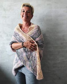 a woman standing in front of a wall wearing a knitted shawl