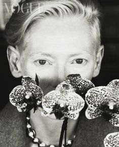 black and white photograph of a young boy with flowers in front of his face, looking at the camera