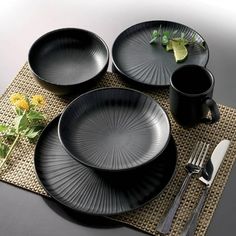 three black plates and two cups on a place mat with silverware next to them