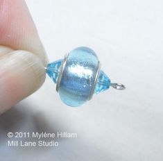 a hand holding a blue glass bead on top of a white surface