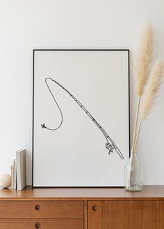 a drawing of a fishing rod on a white wall next to a vase with dry grass in it