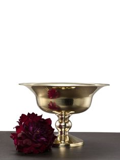 a large metal bowl sitting on top of a wooden table next to a red flower