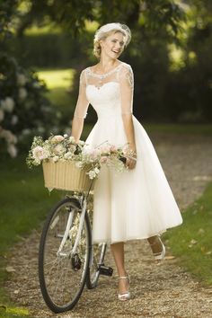 a woman in a white dress is standing next to a bicycle with flowers on it