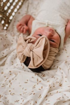 a baby laying on top of a bed wearing a bow tie headband and looking at the camera