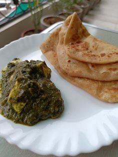 some food is on a white plate and it looks like spinach leaves are next to the pita bread