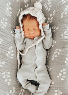 a baby is laying down wearing a knitted hat and sleeping on a blanket with leaves