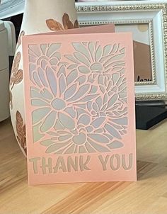 a thank you card sitting on top of a table next to a vase with flowers