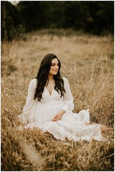 a woman in a white dress is sitting in tall grass and smiling at the camera