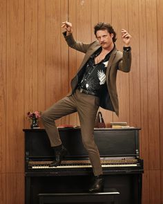 a man standing on top of a piano in front of a wooden paneled wall