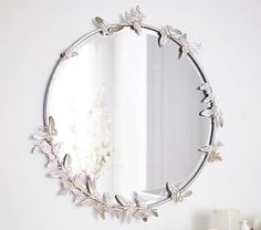 a round mirror hanging on the wall above a white dresser with drawers and vases