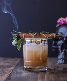 a glass filled with liquid sitting on top of a wooden table next to a skull