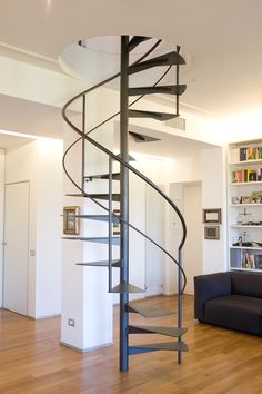 a spiral staircase in the middle of a living room with bookshelves behind it