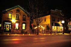 an empty street at night with lights on the buildings and trees in front of it