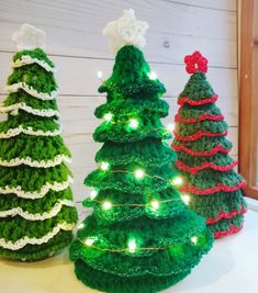 three crocheted christmas trees sitting on top of a white table next to each other