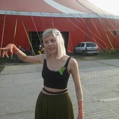 a woman with blonde hair wearing a black top and green skirt standing in front of a tent