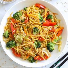 a white bowl filled with noodles, broccoli and carrots next to chopsticks