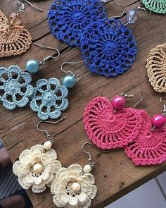 several crocheted earrings are displayed on a wooden table with beads and pearls hanging from them