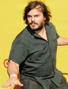 a man with long hair and beard standing in front of a yellow wall holding his arms out