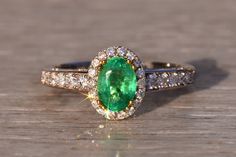 an oval shaped emerald and diamond ring on a wooden surface