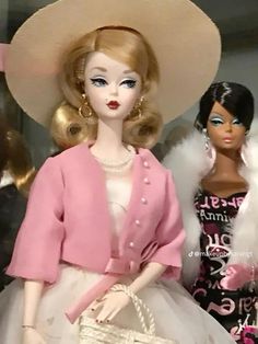 two barbie dolls are standing next to each other in front of a display case wearing dresses and hats