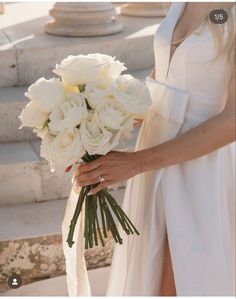 a woman holding a bouquet of white roses in her hand and wearing a wedding dress