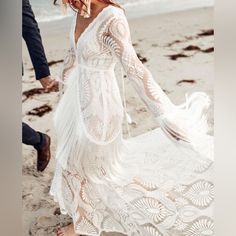 a woman in a white dress is walking on the beach with a man wearing a suit and tie